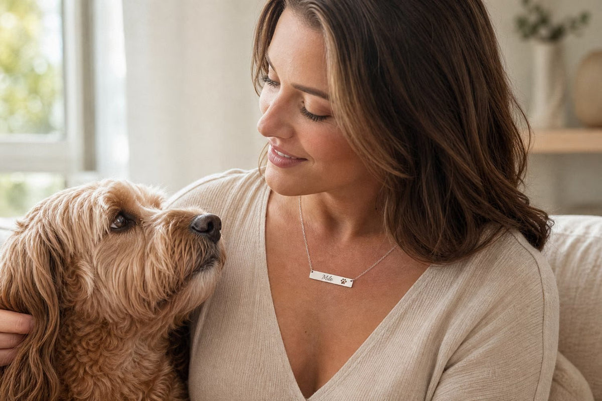 A woman looking at her dog in a lively house, wearing a silver chain with the dog's name on it spelled 'Milo'