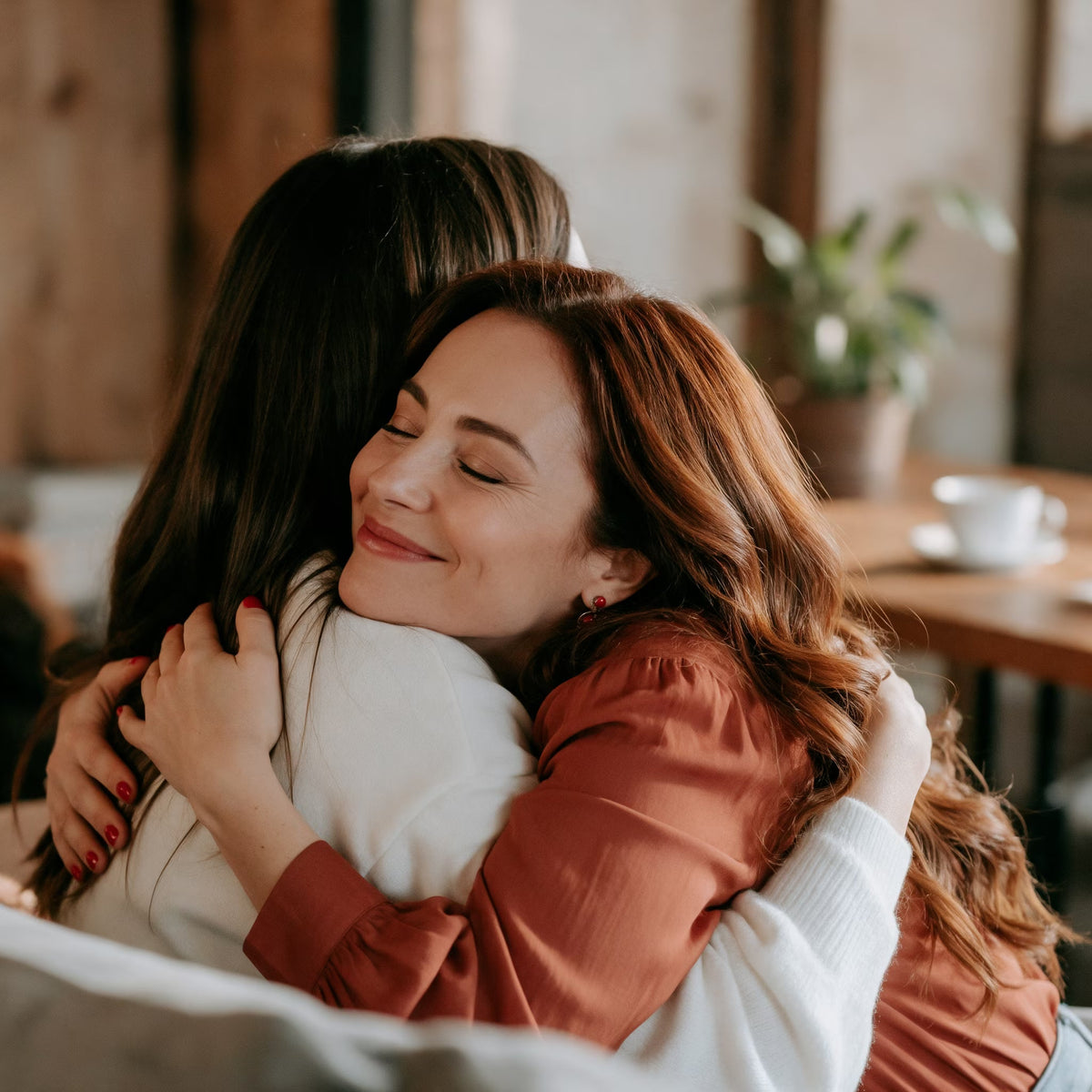A woman with a red shirt hugging a friend inside a cafe