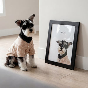 Dog in pajamas standing next to a framed portrait of itself on a wooden floor.