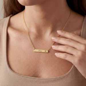 Gold necklace with a nameplate held by a person wearing a beige top.